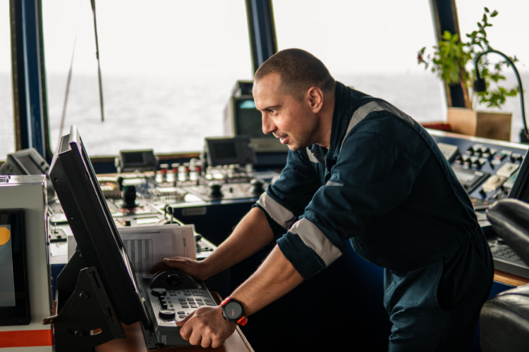 ship captain in a blue uniform operating navigation controls on the bridge of a vessel at sea