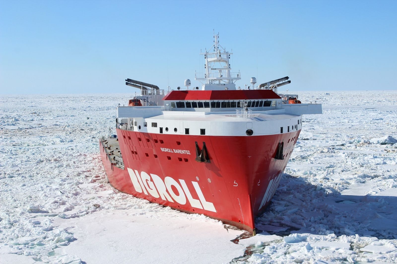 A red icebreaker ship making its way through vast frozen sea covered with thick ice.